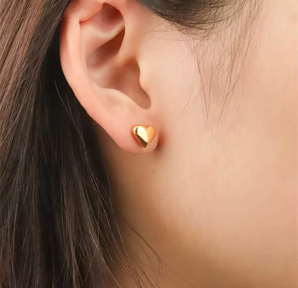 Arete tipo stud de corazón dorado puesto en el lóbulo de la oreja.