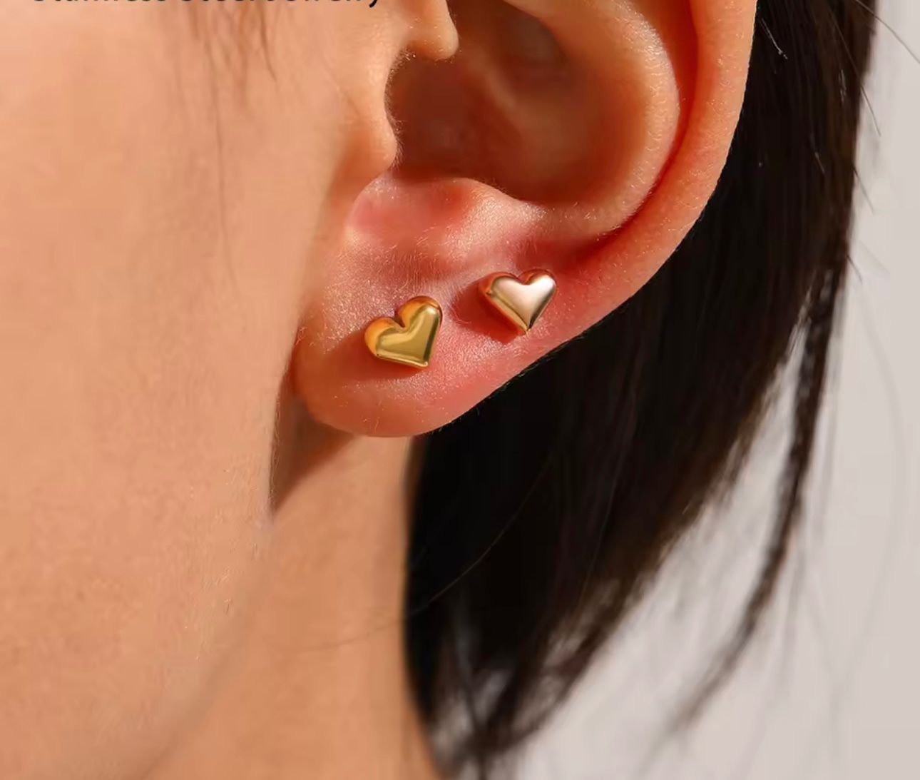 Combinación de dos mini studs de corazón dorados para look de oreja múltiple.